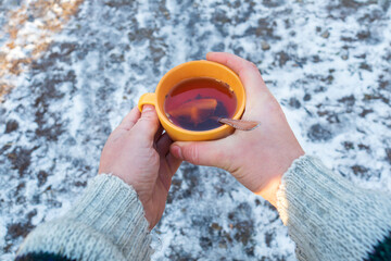 People hands hold an orange mug of hot herbal tea in cold winter. Prevention of viral diseases lemon tea.