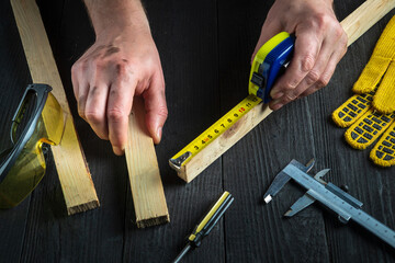 Professional carpenter or woodworker uses a construction tape to measure the length of a piece of...