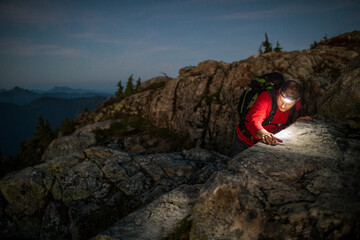 Mountain climber navigates a large boulder at night with headlamp on.
