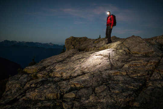 Man hiking on mountain with headlamp aid at night.