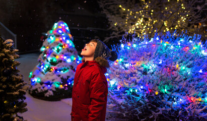 Boy outside at night in the snow with Christmas lights around him.