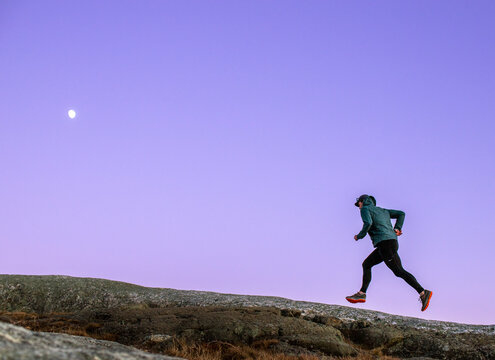 Trail runner climbs mountain with purple sky and moon