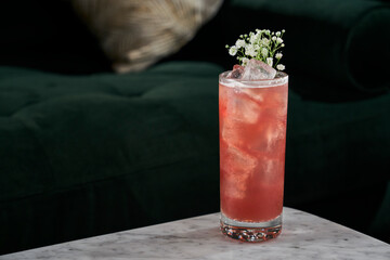 A bright red craft cocktail with flowers for garnish.