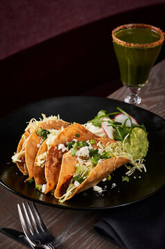 Hard shelled tacos with guacamole and a craft cocktail .