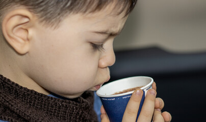 a boy is holding, blowing or drinking a hot chocolate. child drinks from paper cup, cardboard, eco....