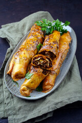 Traditional Turkish crispy sigara borek rolls with minced meat rolled in fillo pastry served as close-up in a Nordic design plate on a black board