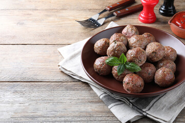 Tasty cooked meatballs with basil served on wooden table. Space for text
