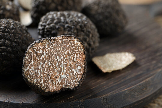 Whole and cut black truffles on wooden board, closeup