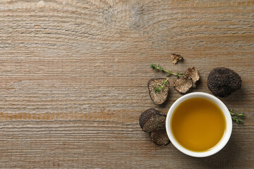 Fresh truffles and oil in bowl on wooden table, flat lay. Space for text