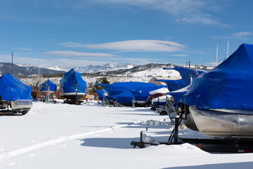 Boats are wrapped and stored for the winter with mountains in the background in Frisco, Colorado with snow on ground.