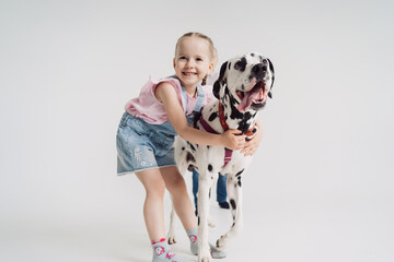 Caucasian little girl playing with a dalmatian dog on white background
