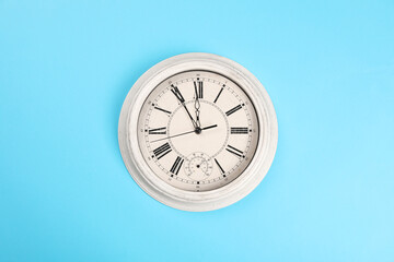 Stylish vintage wall clock showing five minutes until midnight on turquoise background, top view. New Year countdown