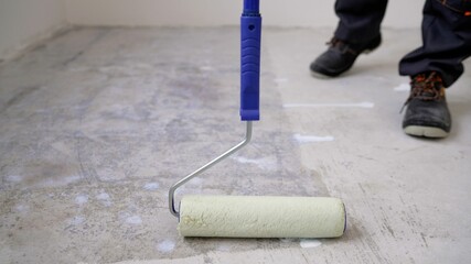 Floor painting, industrial worker with roller and other painting tools. A worker primes the floor...