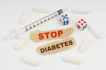 On a white surface lies a syringe, pills, dice and pieces of paper with the inscription - STOP DIABETES
