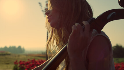 Relaxed girl enjoying performance in sunlight. Young woman embacing contrabass. © stockbusters