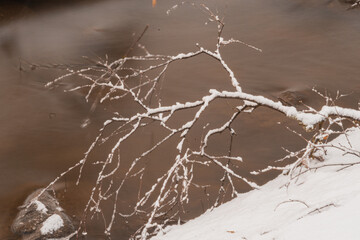 A branch against the background of a stream. a small river in a snowy forest.close-up.. Winter nature.
