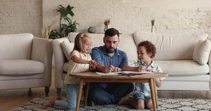 Loving single father his diverse preschooler children drawing pictures with colored pencils in album sit at table at home. Family weekend leisure, creative hobby and pastime, care and custody concept
