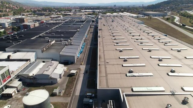 Big factory warehouse rooftop. Aerial drone shot camera flying forward. Factory rooftop, roof windows, ventilation shafts, flat roof of a big factory warehouse. Aerial drone shot camera parallel