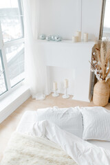 A white bed and a white decorative fireplace. Cozy bright bedroom in minimalism style. Minimalistic trendy interior.