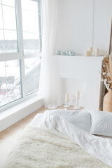 A white bed and a white decorative fireplace. Cozy bright bedroom in minimalism style. Minimalistic trendy interior.