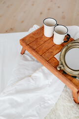 Two white mugs and a newspaper on a breakfast tray, a breakfast concept, a white bed.