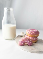 Glazed donuts with milk in a glass bottle on a light background.
