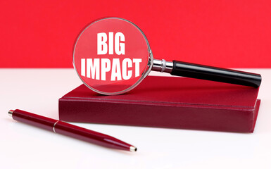 On a white and red background, a notebook, a pen and a magnifying glass, inside which the inscription - Big Impact