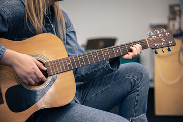 Close-up, a woman in a denim suit plays the guitar.