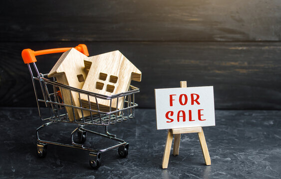 Shopping cart loaded with houses and sign for sale. Buying and selling housing. Saving money in real estate, investing in housing. Property appraisal. Secondary realty market. Attractive prices.