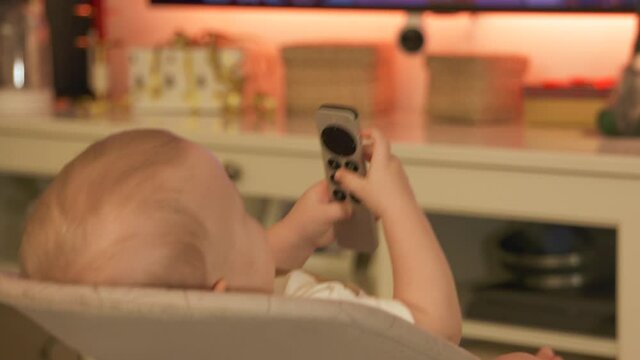 Caucasian small baby watching TV at home, cute little toddler child holding remote control for TV digital media player. High quality 4k footage