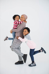 Pleasant african american islamic mother posing with her two happy daughters in studio. Family of three having fun while playing over white background.