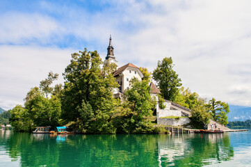 Fototapeta na wymiar Church on an island in the middle of Lake Bled in Slovenia. Church tower illuminated by the sun with reflection in the lake.