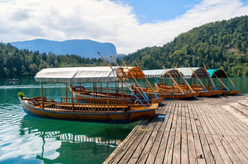 Small wooden boats park in the harbor at the wooden pier on Lake Bled in the Slovenian mountains.