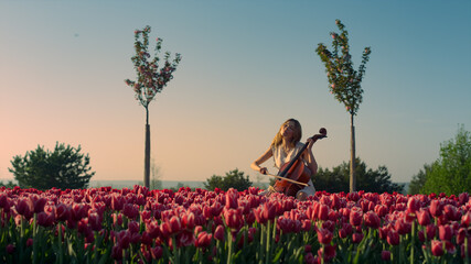 Young woman playing cello with inspiration in blooming tulip field - Powered by Adobe