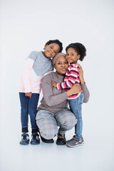 Portrait of happy african islamic woman embracing her little daughters while posing in studio with white background. Two cute sisters spending time with their caring lovely mother.