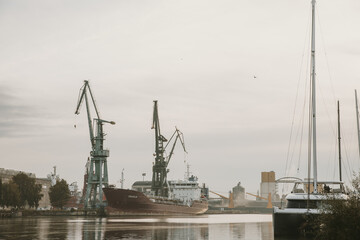 Docks on the Martwa Wisla in Poland city of Gdańsk with docked cargo ship under repair and port cranes in background during cloudy autumn morning