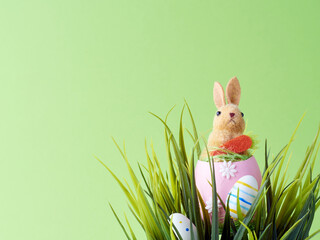 Happy Easter concept. Artificial cute bunny on the shells egg between green grass and green background. 