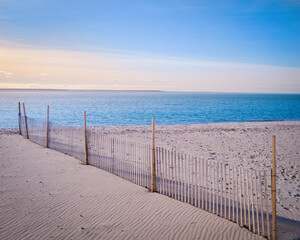 Beach seascape with sand fence, footprints, and wind traces at sunrise on Cape Cod