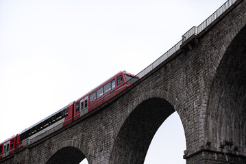 Passenger train crossing stone arch railway bridge in high key
