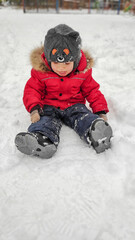 Fototapeta na wymiar Cute little baby child boy in red sport jaket having fun playing on playground, city park outdoors during snowfall in winter. Children winter seasonal outdoor activities