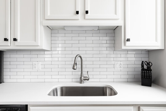 Kitchen sink detail shot with a subway tile backsplash, granite countertop, white cabinets, and a chrome faucet.
