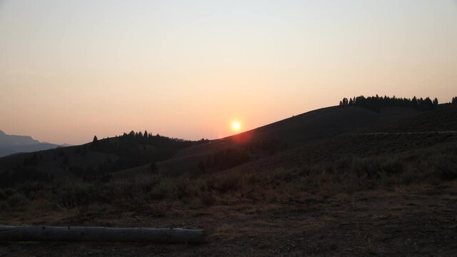Time-lapse of the sun setting behind a hill on 'Nip and Tuck Road' north of Stanley, Idaho in the Sawtooth National Recreation Area on a summer evening. The sun is reddish due to forest fire smoke.