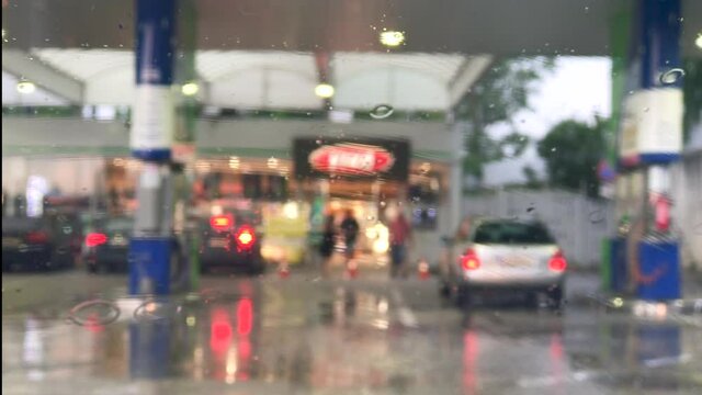 Blurred background of the gas station, Raindrops on the car window. Wiper moves.