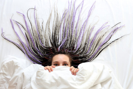 Young women with dreadlocks is peeping out under the blanket