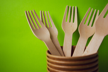 Set of disposable wooden forks in a paper cup on a green background. Eco friendly organic tableware with space for text. Disposable kitchen cutlery. Utensils made of bamboo wood copy space. Zero waste