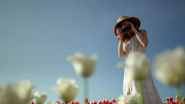 Beautiful girl with photocamera laughing in tulip field. Woman taking pictures. 