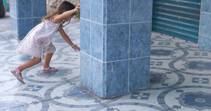 Cute little girl stumbling while playfully running around blue-tiled column