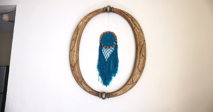 Beautiful blue dreamcatcher hanging from wooden frame on white wall