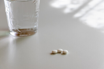 窓際のテーブルに置かれた白い錠剤とグラスの水