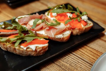 bruschetta with salmon, cottage cheese, dried tomatoes and micro greens, on a black background